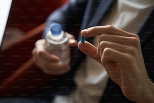 Persona sosteniendo el medicamento en una píldora azul entre los dedos con una botella de agua en la otra mano