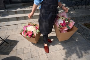 Cropped photo of a florist in an apron carrying chic bouquets of flowers in bags down the street
