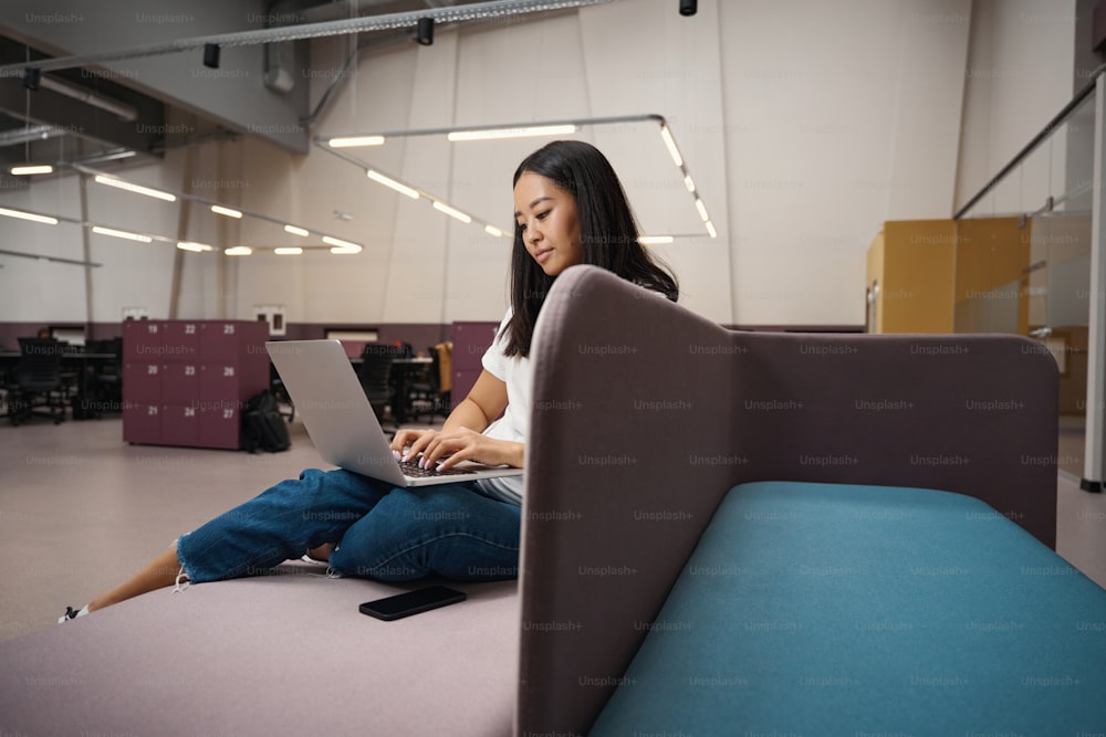 Ritratto della vista laterale dell'allegro impiegato asiatico sta usando internet mentre lavora sul laptop nell'ufficio più grande
