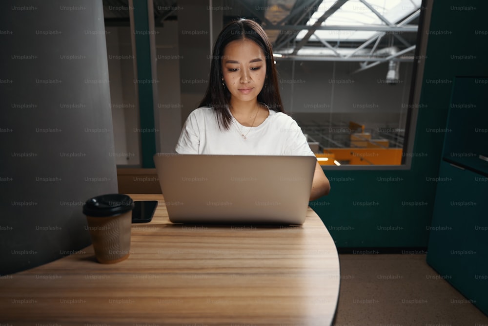 Ritratto della vista frontale di bella imprenditrice concentrata sta lavorando sul computer portatile mentre utilizza Internet nel posto di lavoro moderno