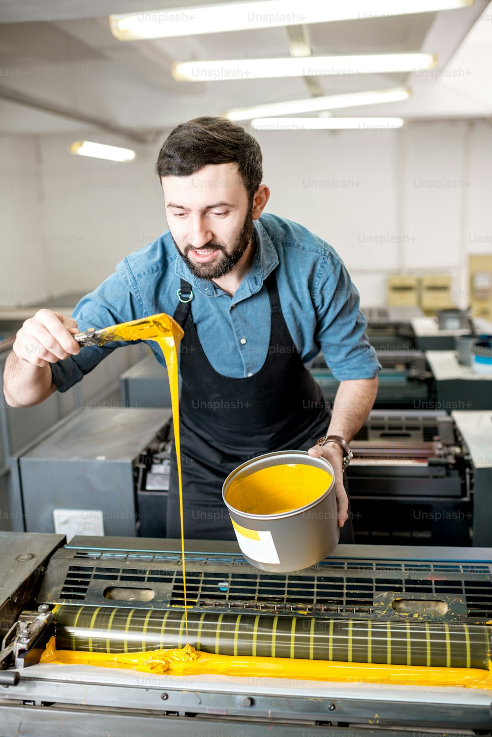 타이포그래퍼가 인쇄 제조 공정에서 오프셋 기계에 노란색 페인트를 채우고 있다