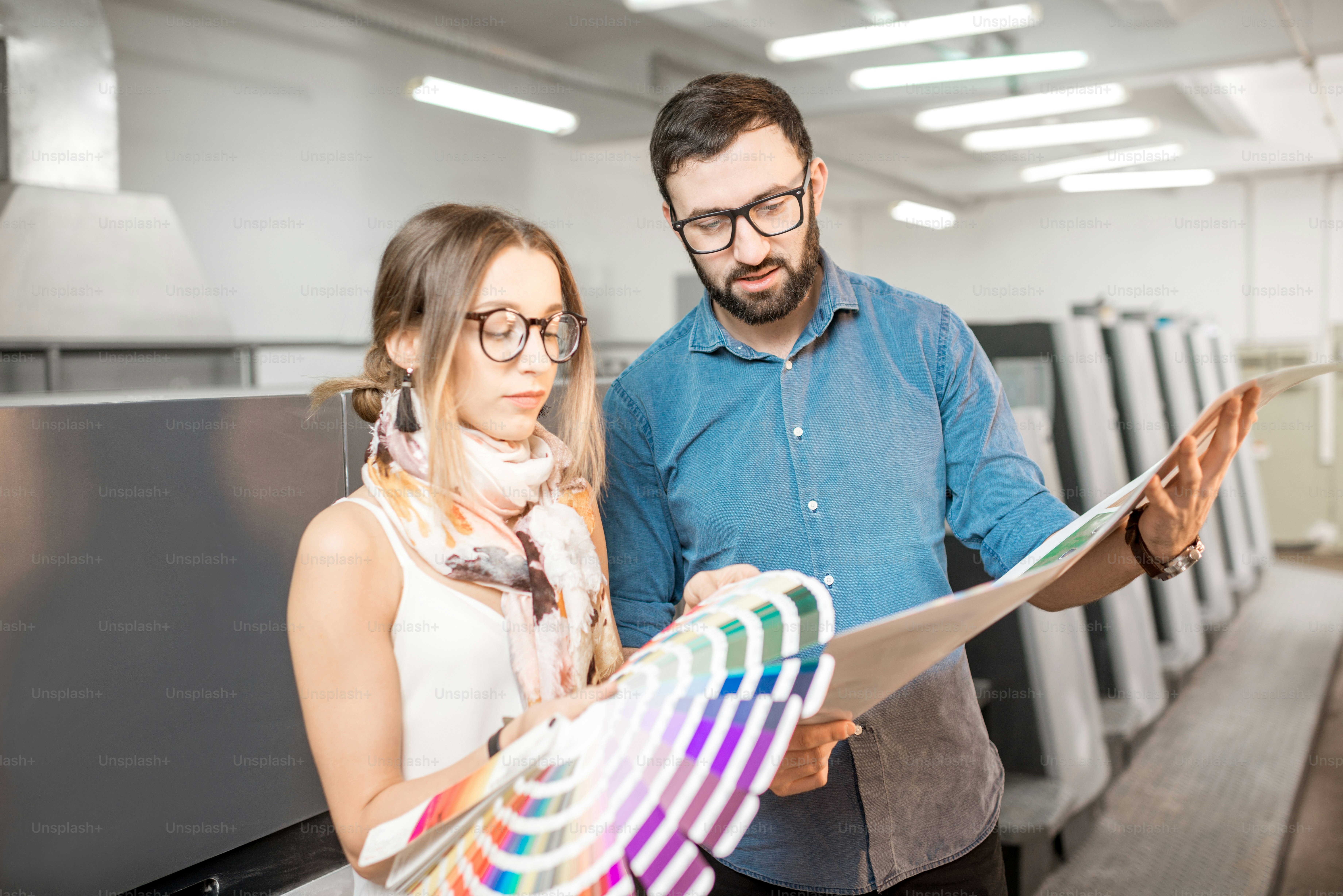 Young woman designer and print operator working together with color swatches standing at the print manufacturing