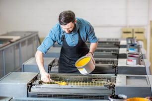 Tipógrafo llenando pintura amarilla en la máquina offset en la fabricación de impresión