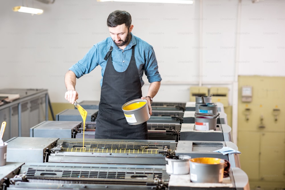 Typographer filling yellow paint into the offset machine at the printing manufacturing