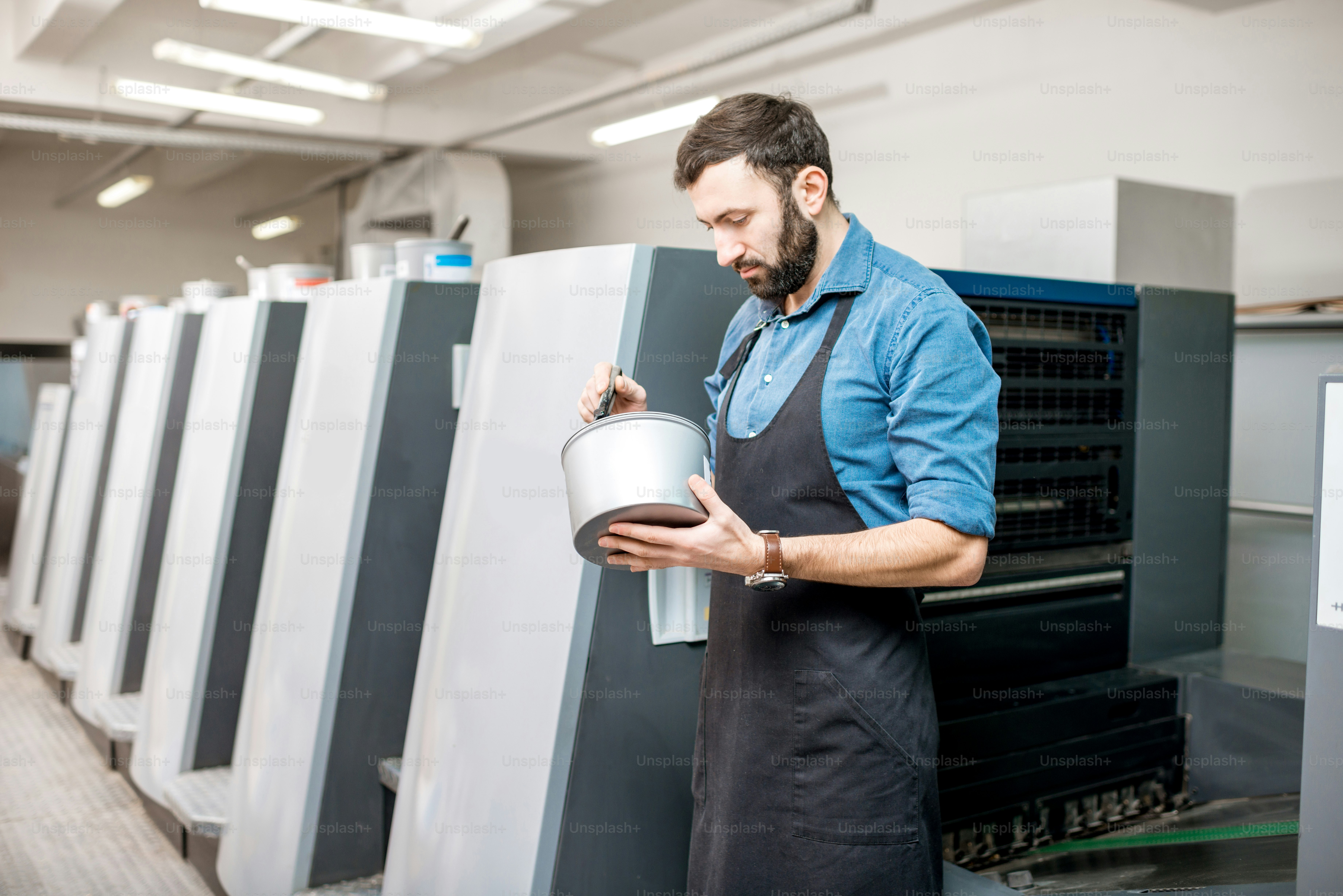 Typographer stiring paint for offset machine standing at the printing manufacturing