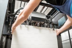 Trabajador llenando las hojas de papel para imprimir en la máquina de impresión offset en la fabricación