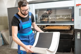 Travailleur en unifrom obtenant des feuilles imprimées de la machine offset à l’imprimerie