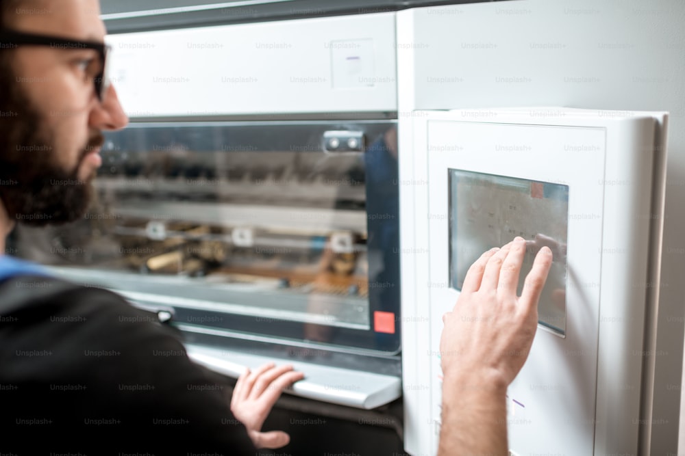 Homem operando a máquina offset empurrando a tela sensível ao toque na fabricação de impressão. Vista em close-up