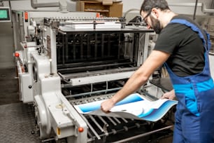 Tipógrafo comprobando la calidad de impresión de pie cerca de la vieja máquina de prensa en la fabricación de impresión