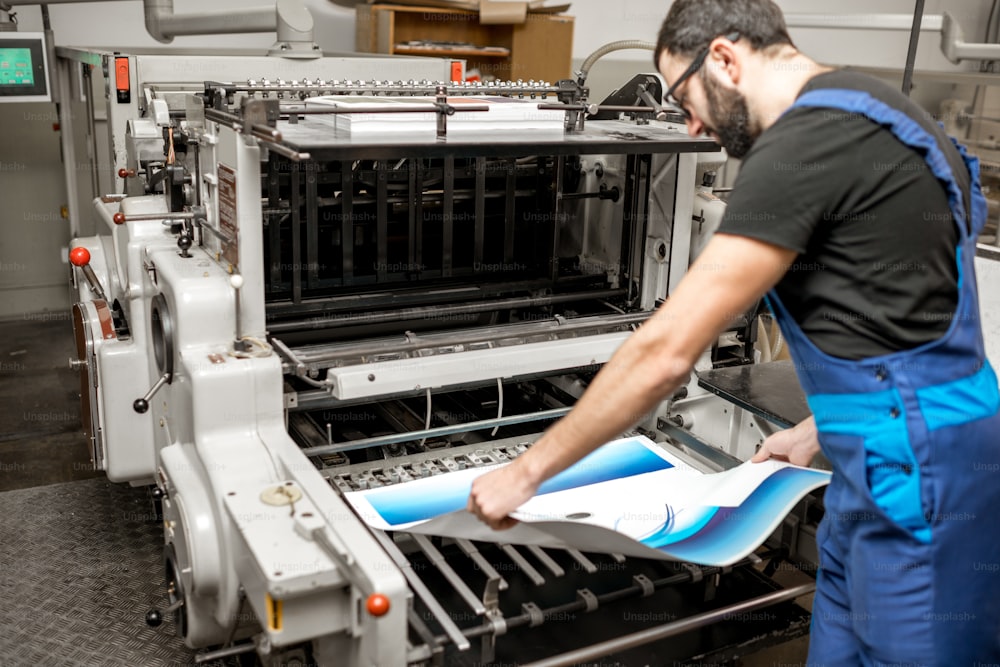 Tipografo che controlla la qualità di stampa in piedi vicino alla vecchia macchina da stampa presso la produzione di stampa