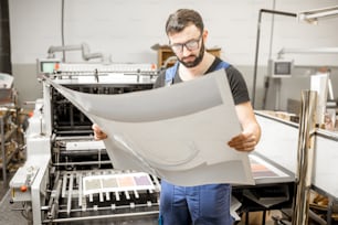 Tipógrafo verificando a qualidade de impressão em pé perto da máquina de impressão antiga na fabricação de impressão