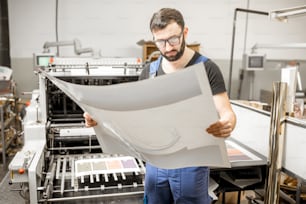 Typographer checking printing quality standing near the old press machine at the printing manufacturing