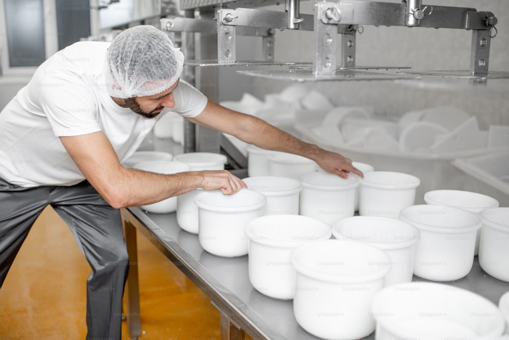 Hombre en uniforme formando queso en los moldes de plástico poniéndolos bajo la prensa en la fabricación de queso