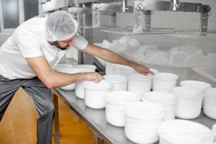 L'uomo in uniforme forma il formaggio negli stampi di plastica mettendoli sotto la pressa alla produzione del formaggio