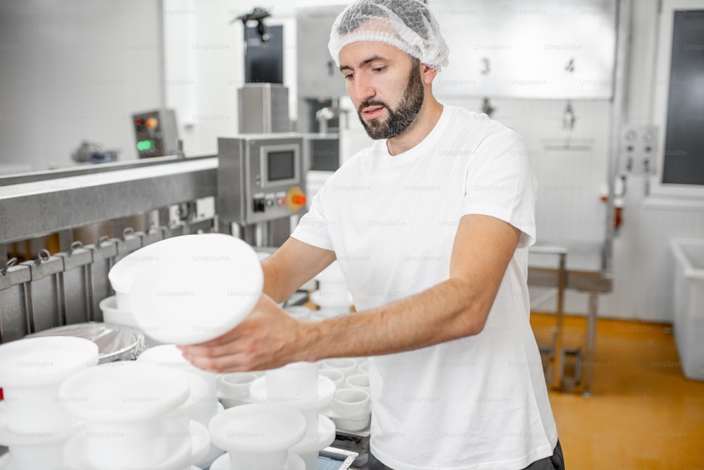 Hombre en uniforme formando queso en los moldes de plástico poniéndolos bajo la prensa en la fabricación de queso