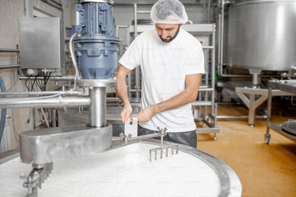 Homem misturando leite no tanque inoxidável durante o processo de fermentação na fabricação de queijo