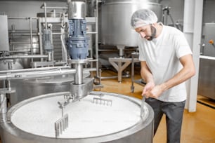 Mann mischt Milch im Edelstahltank während des Fermentationsprozesses in der Käseherstellung