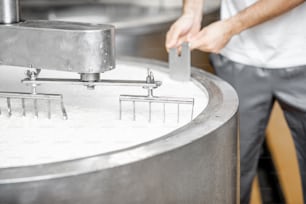 Homem misturando leite no tanque inoxidável durante o processo de fermentação na fabricação de queijo. Vista de perto sem rosto