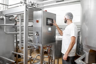 Worker operating pasteurizer using the control panel at the cheese or milk manufacturing