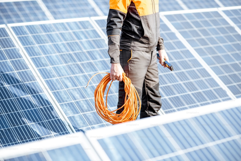 Trabalhador bem equipado em roupas laranja protetoras que servem painéis solares em uma usina fotovoltaica no telhado. Conceito de manutenção e instalação de estações solares