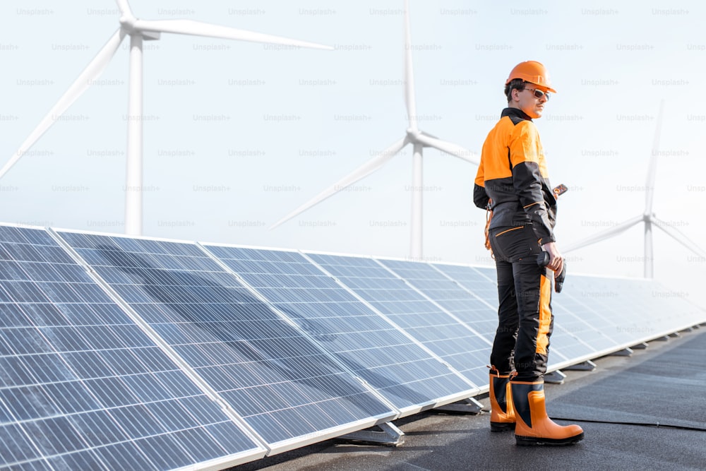 Well-equipped worker in protective orange clothing examining solar panels on a photovoltaic rooftop plant. Concept of maintenance and installation of solar stations
