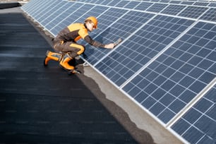 Well-equipped worker in protective orange clothing installing solar panels, measuring the angle of inclination on a photovoltaic rooftop plant