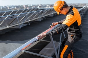 Lavoratore ben attrezzato in abbigliamento protettivo arancione che installa o sostituisce il pannello solare su un impianto fotovoltaico sul tetto. Concetto di manutenzione e installazione di stazioni solari