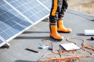 Installazione di pannelli solari, primo piano su uno strumento di lavoro. fili e uomo in indumenti protettivi in piedi su un tetto con centrale fotovoltaica