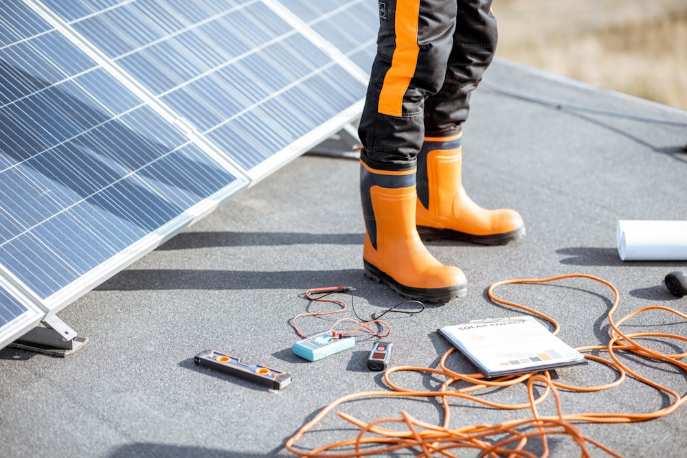 Installazione di pannelli solari, primo piano su uno strumento di lavoro. fili e uomo in indumenti protettivi in piedi su un tetto con centrale fotovoltaica