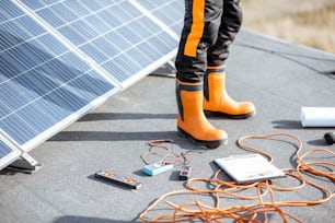 Installing solar panels, close-up on a working tools. wires and man in protective clothing standing on a rooftop with photovoltaic power station