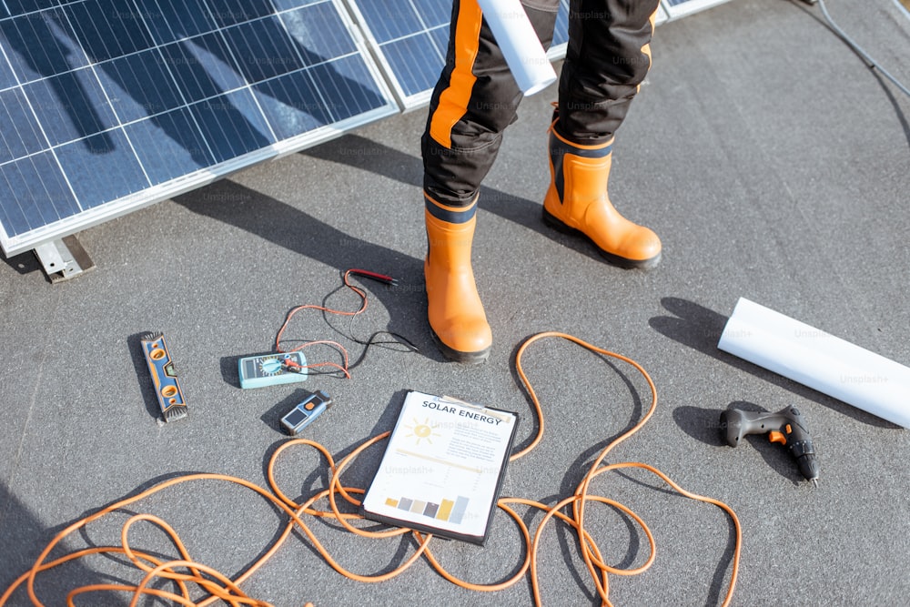 Installation de panneaux solaires, gros plan sur un outil de travail. Des fils et un homme en vêtements de protection debout sur un toit avec une centrale photovoltaïque