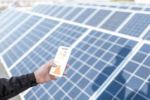 Homem examinando a genaração da usina de energia solar, segurando um telefone inteligente com gráfico de produção de eletricidade. Conceito de monitoramento online da estação elétrica