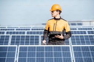 Engenheiro em vestuário de trabalho de proteção realizando serviço de painéis solares com tablet digital em uma planta de telhado fotovoltaico. Conceito de manutenção e configuração de estação de energia solar