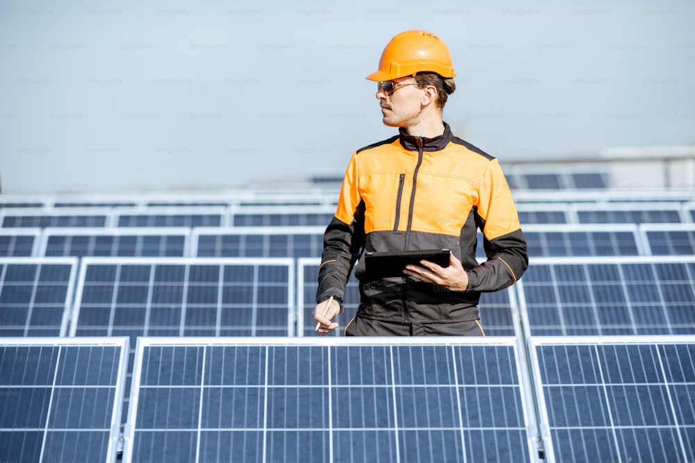 Ingeniero en ropa de trabajo de protección realizando servicio de paneles solares con tableta digital en una planta fotovoltaica en techo. Concepto de mantenimiento y configuración de la estación de energía solar