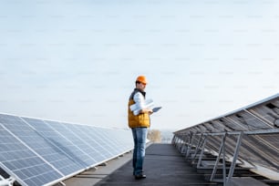 View on the rooftop solar power plant with mann walking and examining photovoltaic panels. Concept of alternative energy and its service