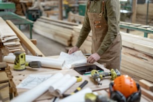 Artesano diseñando algo de carpintería en el banco de trabajo con herramientas y planos en la carpintería. Foto de alta calidad