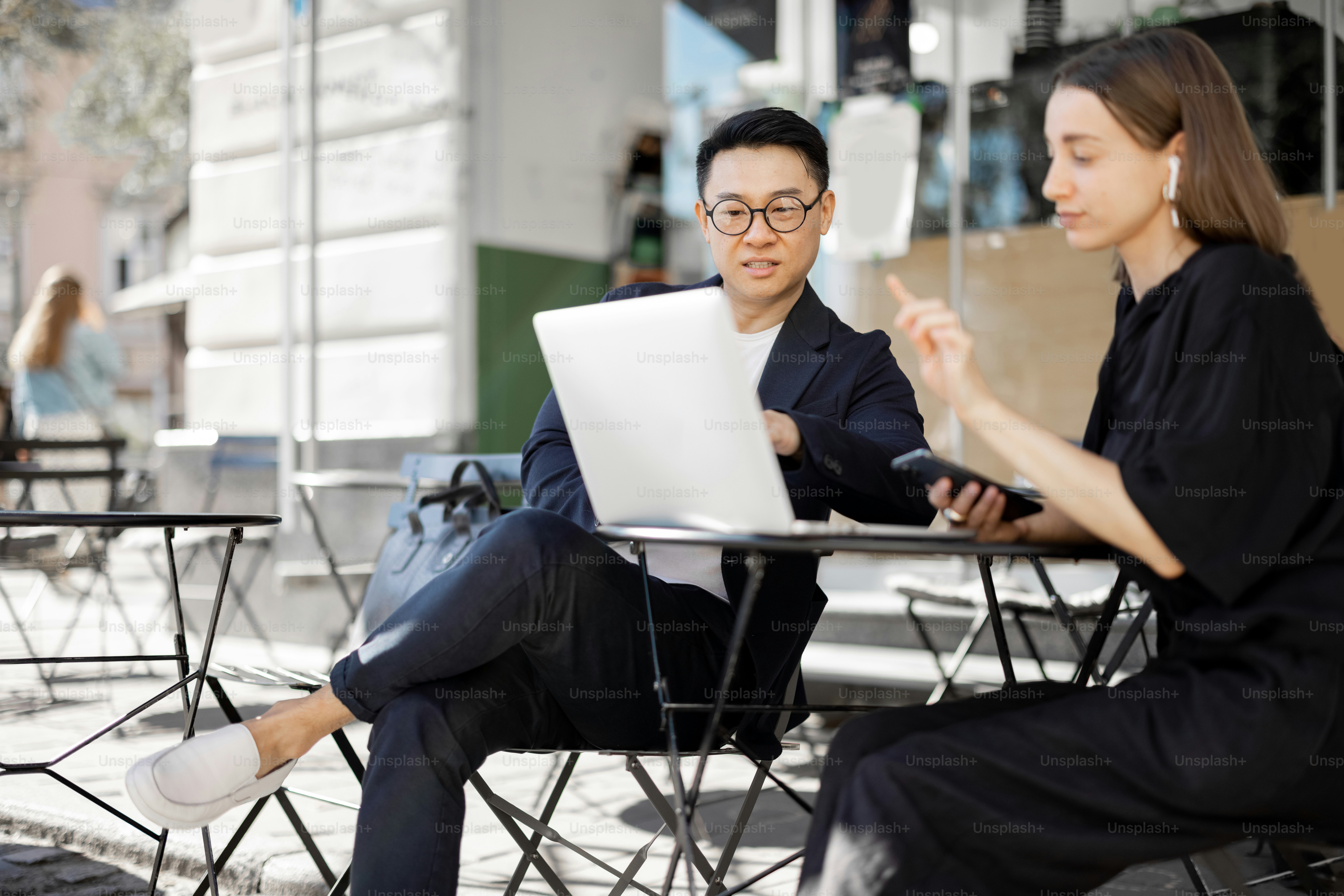 Multiracial business people watching something on laptop during work at outdoor cafe. Concept of remote and freelance work. Idea of teamwork and business cooperation. Caucasian woman with smartphone