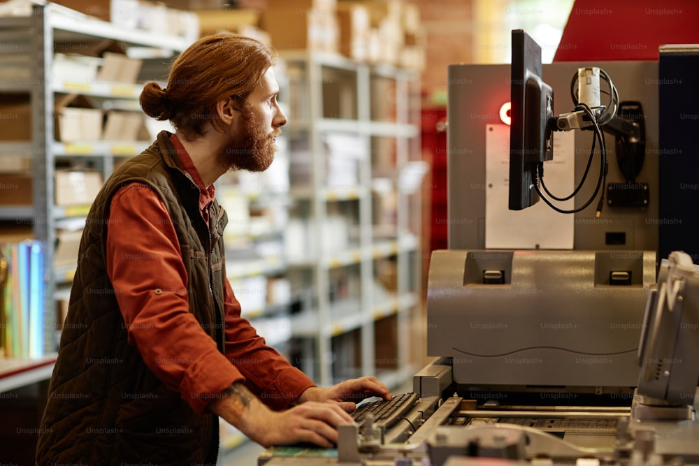 Retrato da vista lateral do trabalhador do sexo masculino que opera a máquina de impressão na fábrica de impressão