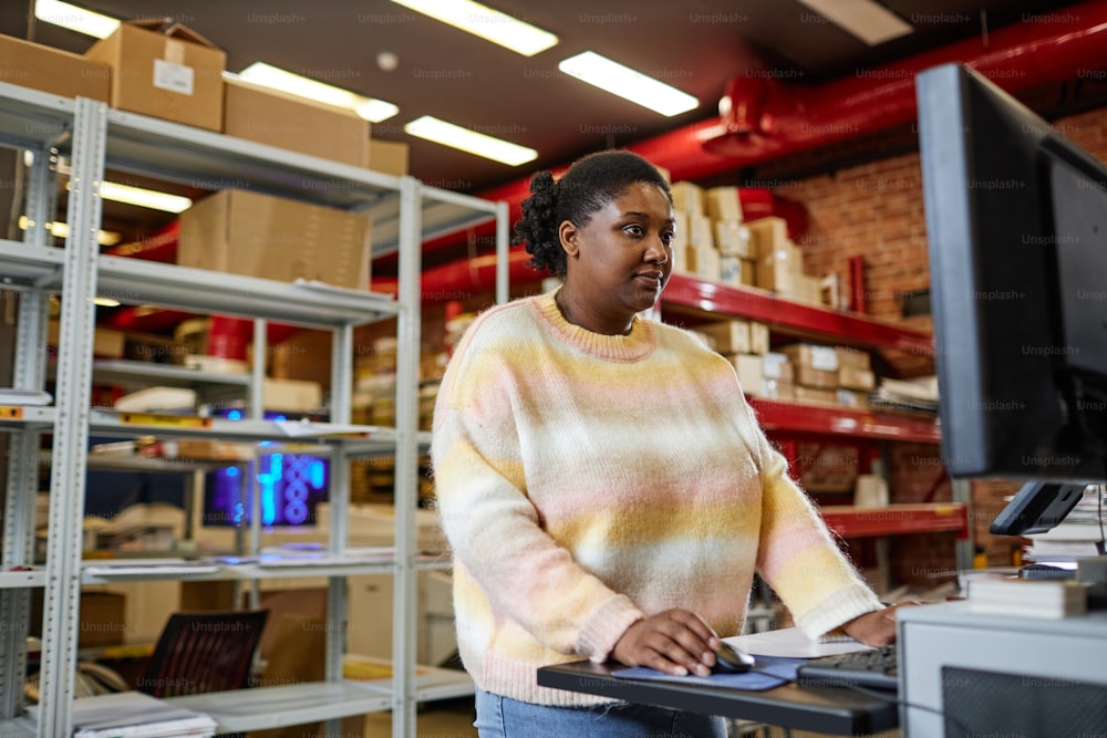 Ritratto della vita della donna nera adulta che utilizza il computer durante l'impostazione delle macchine da stampa nel negozio industriale, spazio di copia