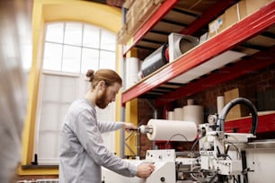 Vue latérale portrait d’un jeune homme mettant du matériel dans une machine d’impression industrielle à l’atelier, espace de copie