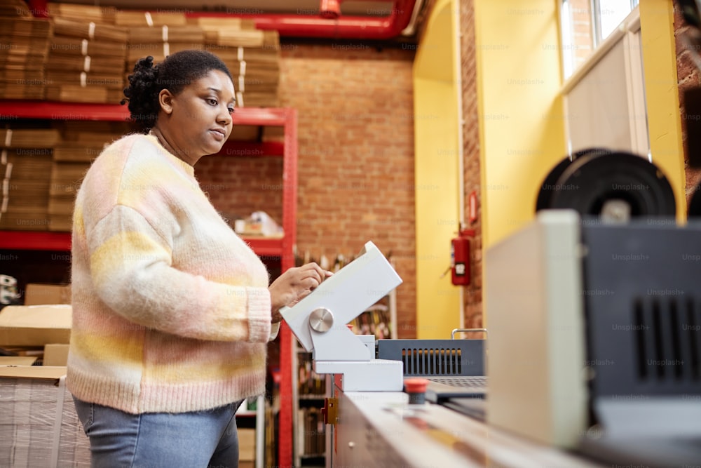 Ritratto laterale della donna nera adulta che gestisce la macchina da stampa industriale in officina, spazio di copia