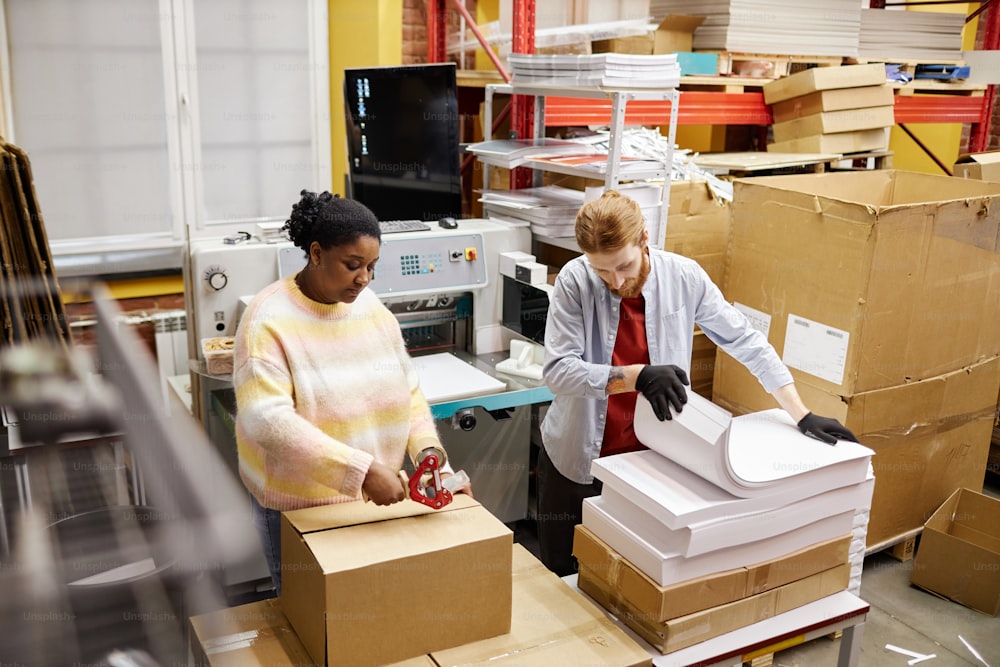 Winkelansicht von Arbeitern, die Kartons mit Papier in einer industriellen Druckerei öffnen, Kopierraum