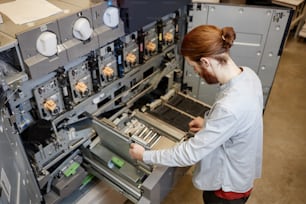 Retrato de alto ángulo joven trabajando en una imprenta industrial y configurando máquinas, espacio de copia