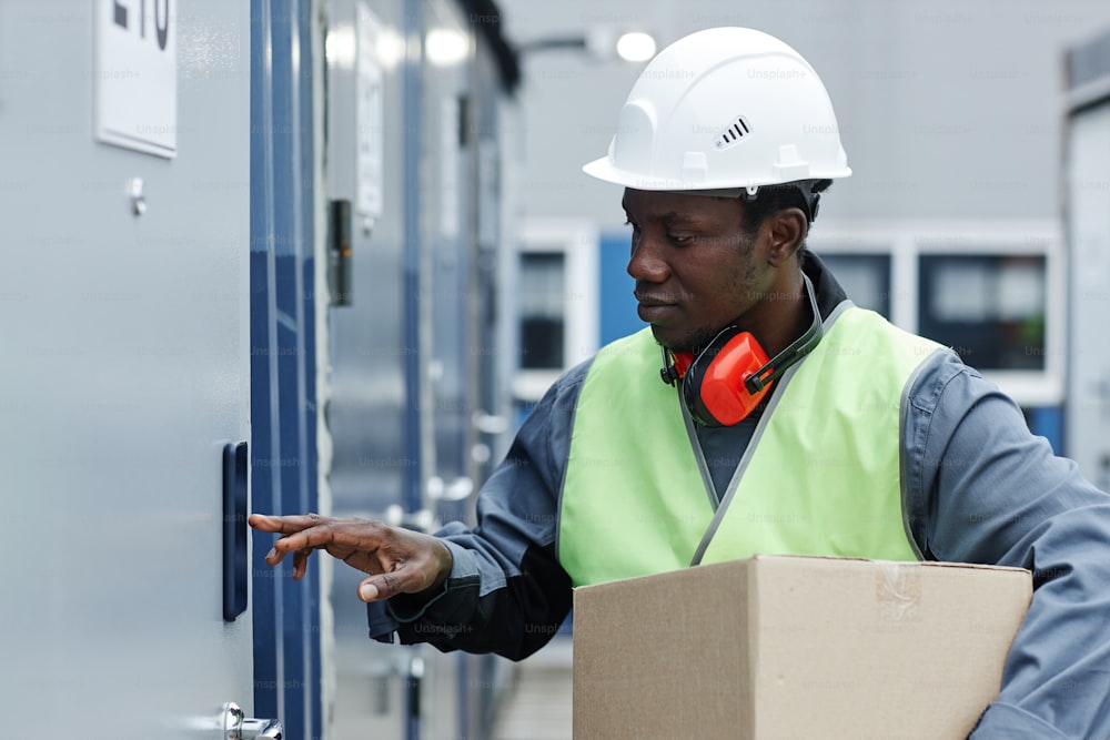 Side view portrait of black young man wearing hardhat while entering code on storage unit