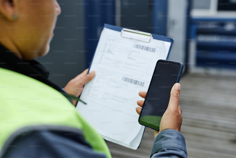 Copy space of unrecognizable worker holding clipboard and smartphone in shipping docks, copy space
