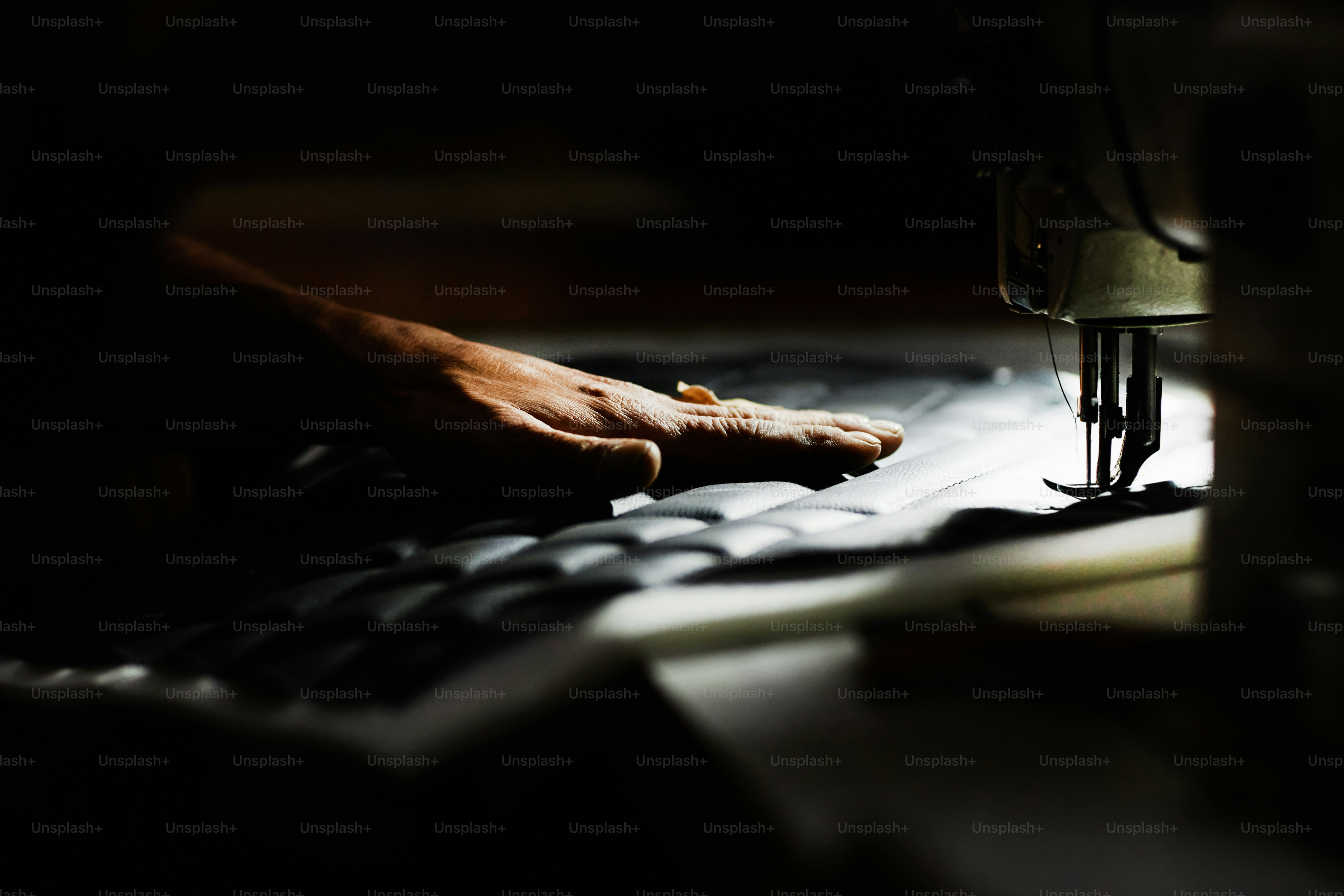 Close up of person sewing car upholstery detail with industrial sewing machine, focus on hand in accent light