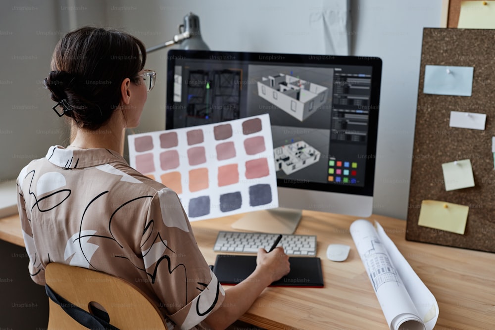 Designerin hält Farbmuster in der Hand, während sie am Arbeitsplatz mit dem Computer arbeitet