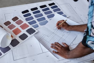 Gros plan d’un architecte masculin travaillant sur des plans d’étage et des échantillons de couleurs pour un projet de design d’intérieur