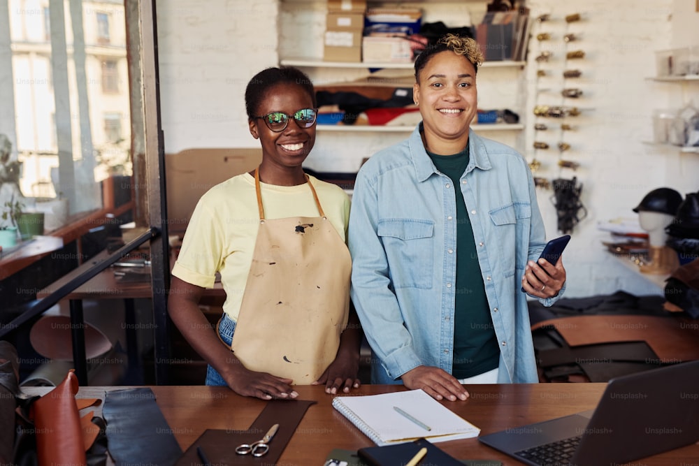 Portrait of two female business partners smiling at camera while posing in leatherworking workshop, copy space