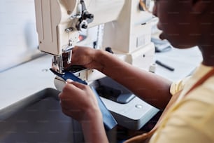 Nahaufnahme einer schwarzen jungen Frau, die eine Nähmaschine benutzt, während sie eine handgefertigte Ledertasche entwirft
